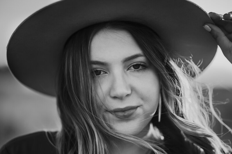 Senior girl holds on to hat in black and white photo while the wind blows
