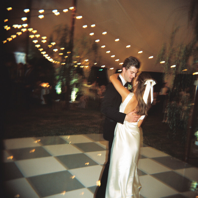 Bride and groom dancing on a checker dance floor under a tent and string lights