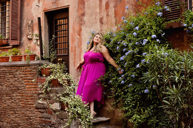A beautiful girl in a fuschia dress leaning against a roman building with ivy. Taken by Rome Solo  Travel Photographer, Tricia Anne Photography