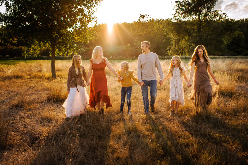 Family of six holding hands walking towards camera in pretty light