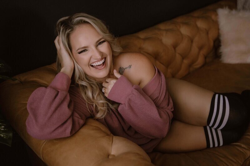 blonde woman with tattoo wearing a Mauve sweater knee high black tube socks  laughing