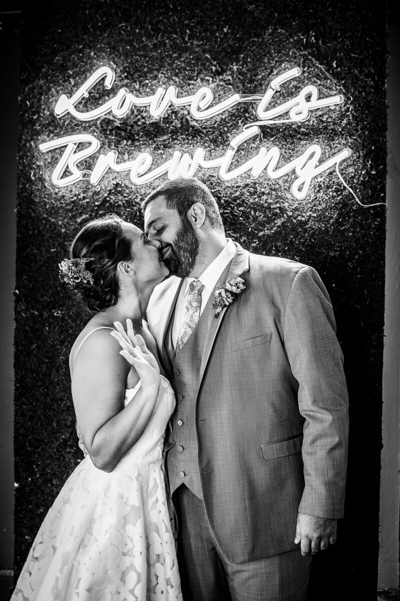 A bride and groom kissing in front of a neon sign