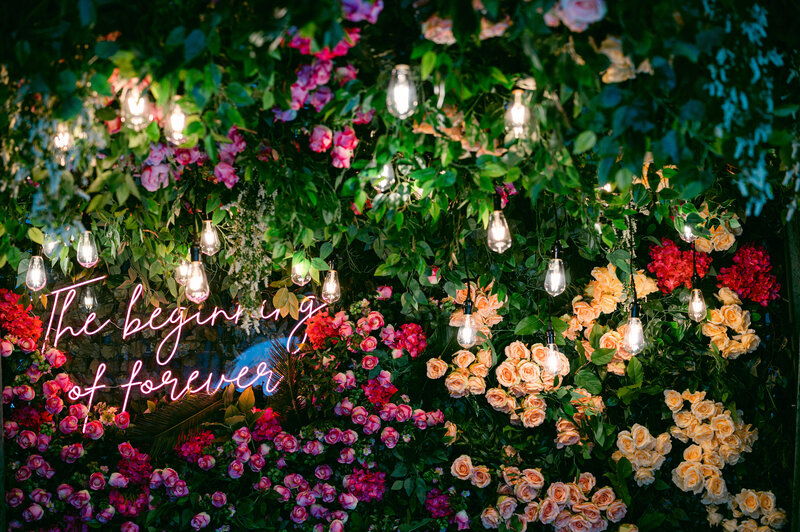 a pink neon sign over a floral grass wall