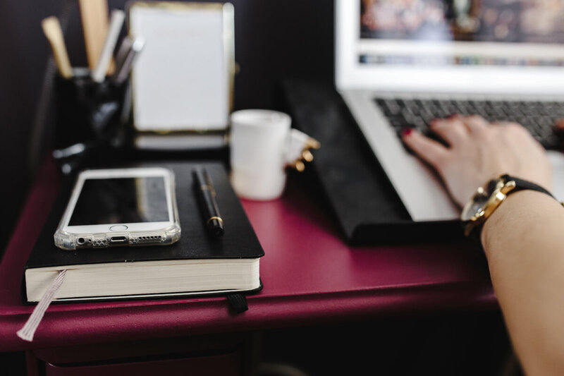 Working at her magenta desk, a woman types on her laptop while her planner and fountain pen sit nearby.