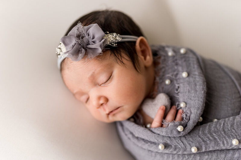 newborn baby girl holding a heart and wearing a headband