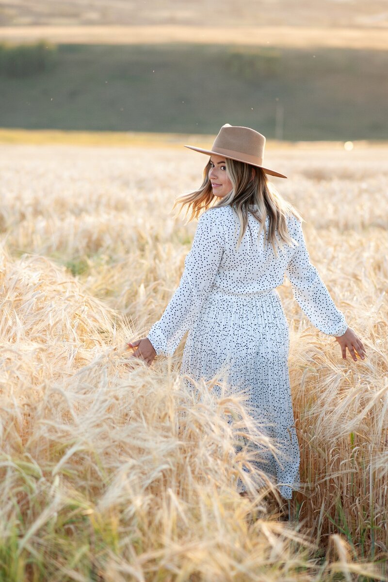 Woman walking through a wheat field by Calgary portrait photographer Tara Whittaker.