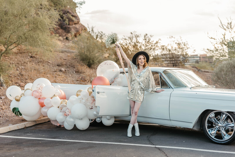 Bride holds bouquet up while leaning on vintage car