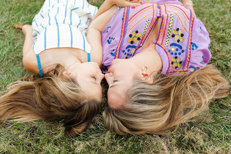 A mom and daughter laying in the grass while holding hands.