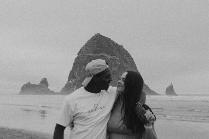 Brooke and David Pitchford  with arms around each other looking sweetly at each other in front of haystack rock