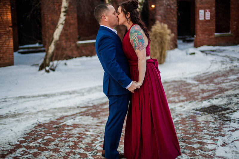 Couple kissing in the middle of snow covered brick path in Modern Tool Square