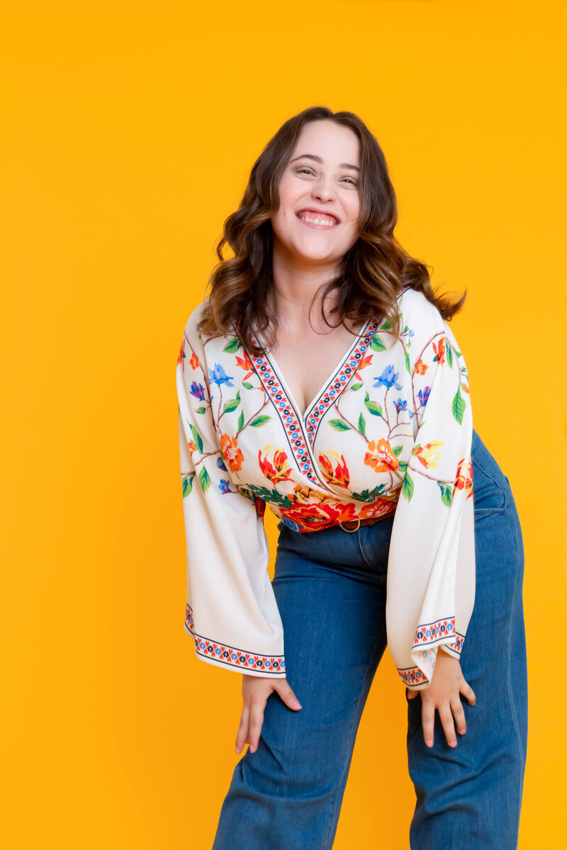 Woman in embroidered top laughing on yellow backdrop
