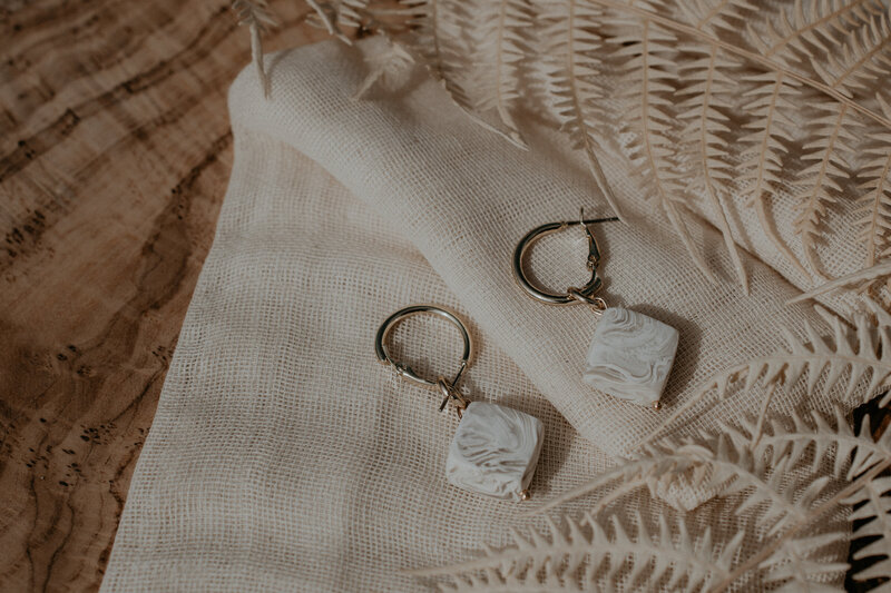 Estelle By Chloe clay handmade earrings laying on cheese cloth with dried florals