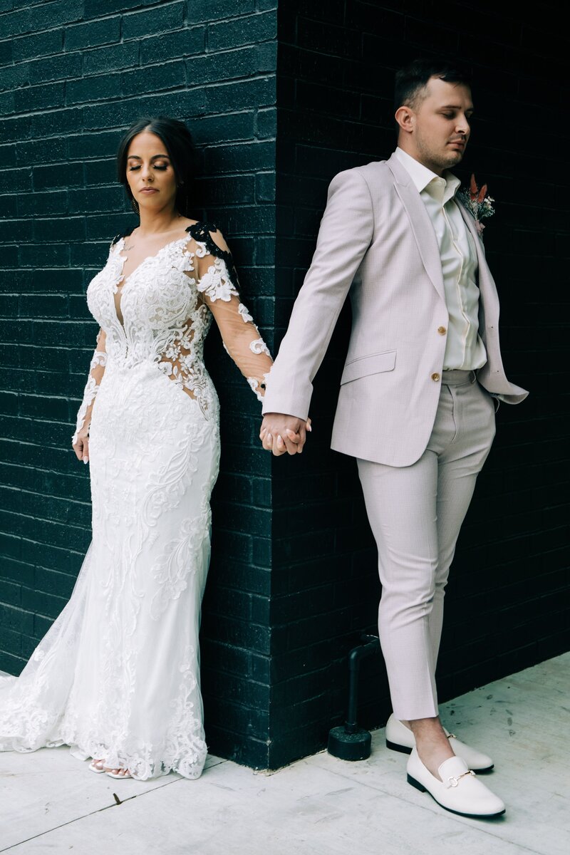 A bride and groom holding hands in front of a brick wall, captured by destination wedding photographer Britt Elizabeth