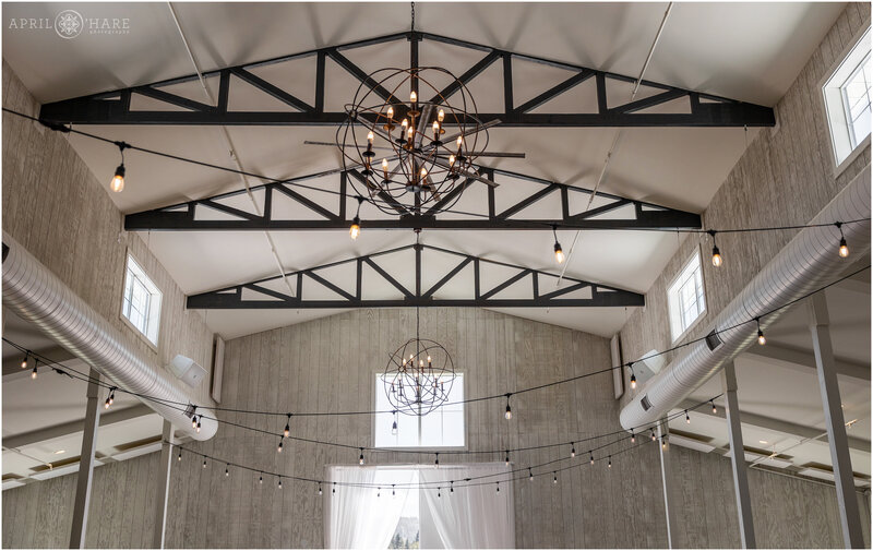 Newly built modern barn wedding venue with tall ceilings, white washed wood walls, black beams and modern chandeliers