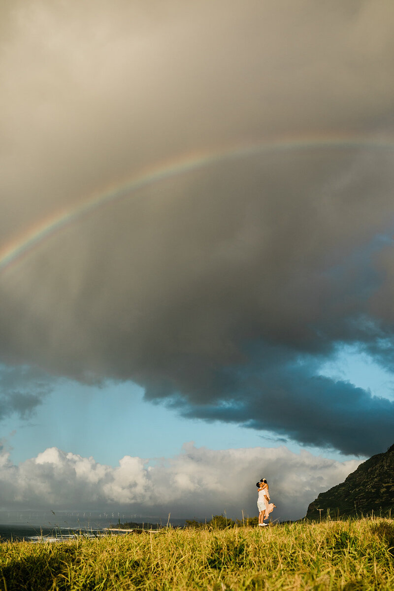 man lifting woman up for a kiss in front of a rainbow for engagement