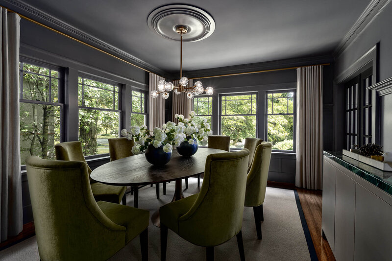 Marguerite Project, a grey dining room with a wooden oval table, green chairs, and lots  of windows