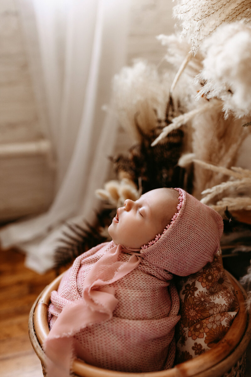 Newborn baby girl wrapped in a pink blanket with a matching hat.