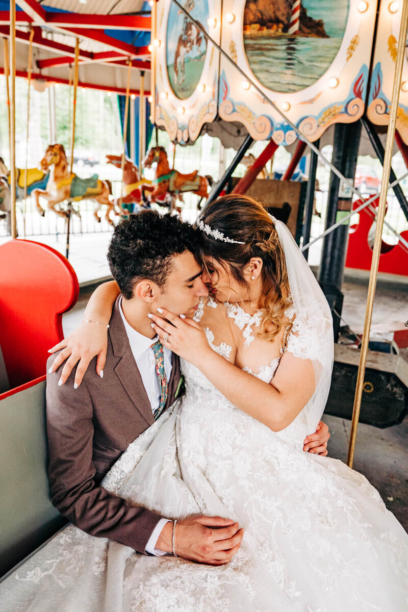 A wedding couple lean in for a kiss on a carousel  at their unique wedding venue in Michigan.