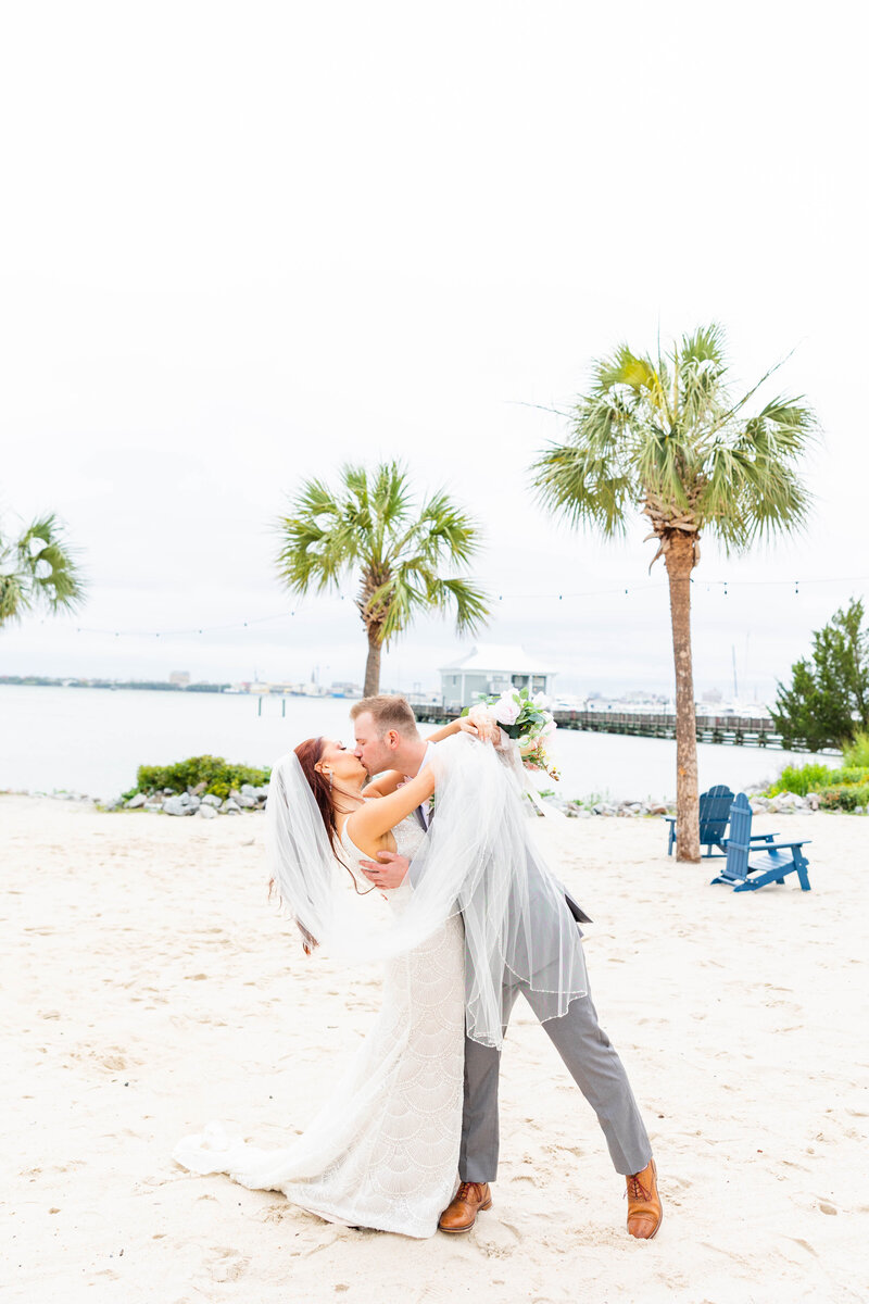 groom dipping bride back and kissing her with water and palm trees in the background
