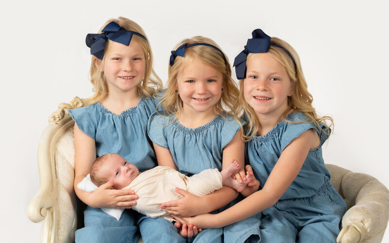 Big Sisters holding Newborn baby brother for a  Photo wearing Jean Jumpers