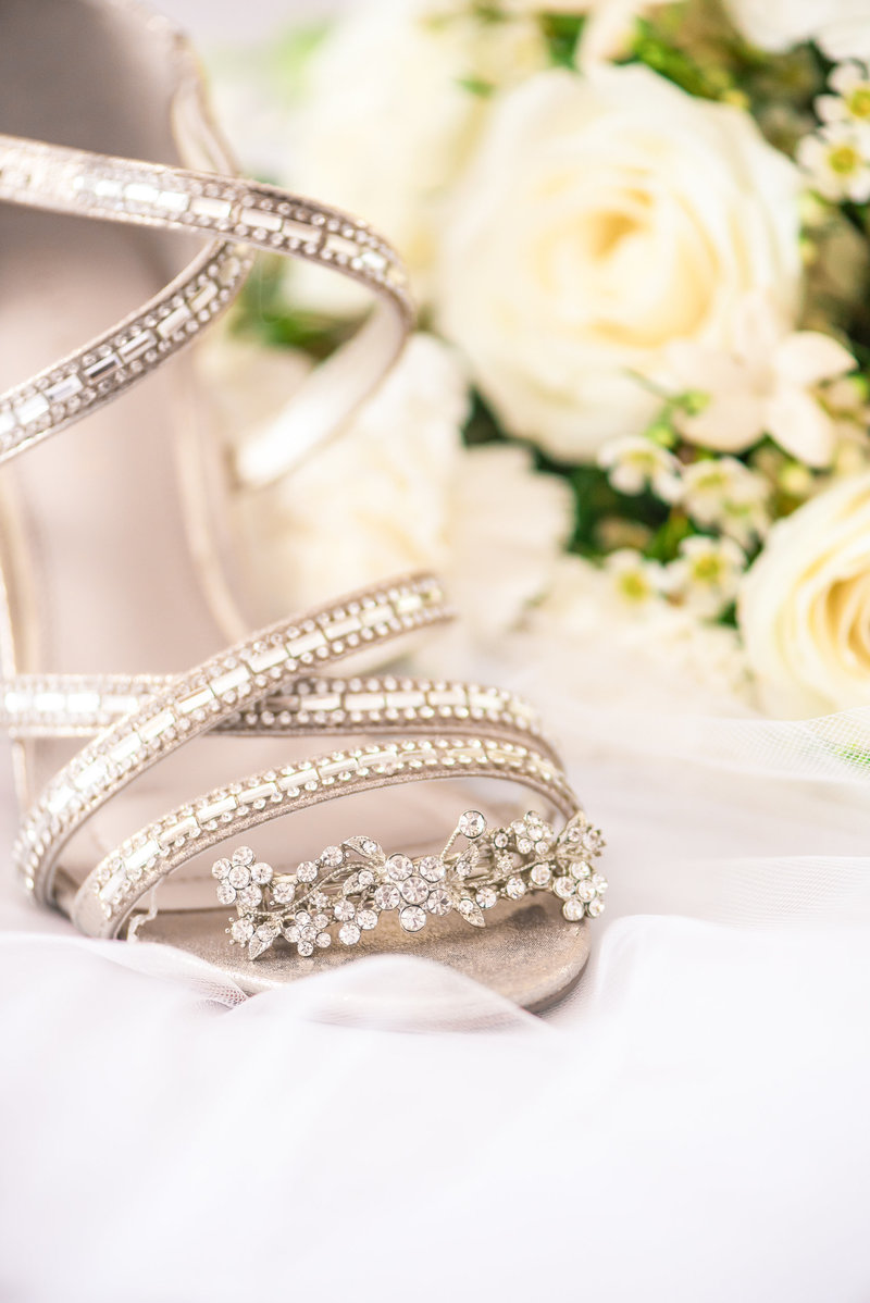 A Decorative crystal hairpiece rests ion the toe of a bride's shoe