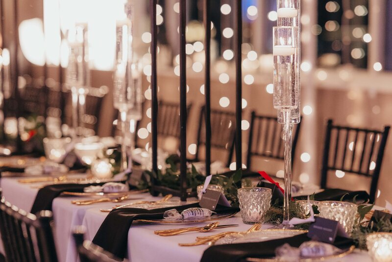 Elegant wedding banquet table setup with crystal candle holders, gold cutlery, and twinkling lights in the background.