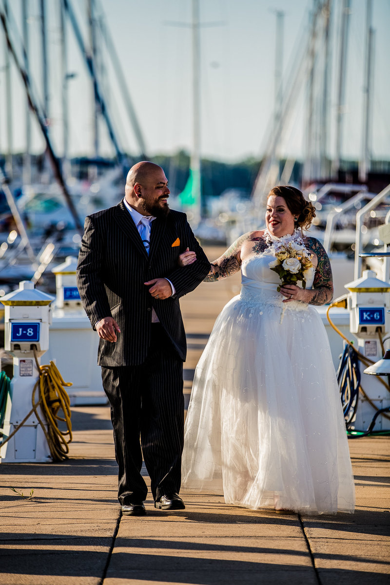 Bride and groom walk arm in arm along the dock at the Erie Yacht Club