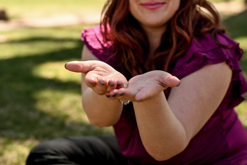 A woman is sitting on grass with her hands out in front of her