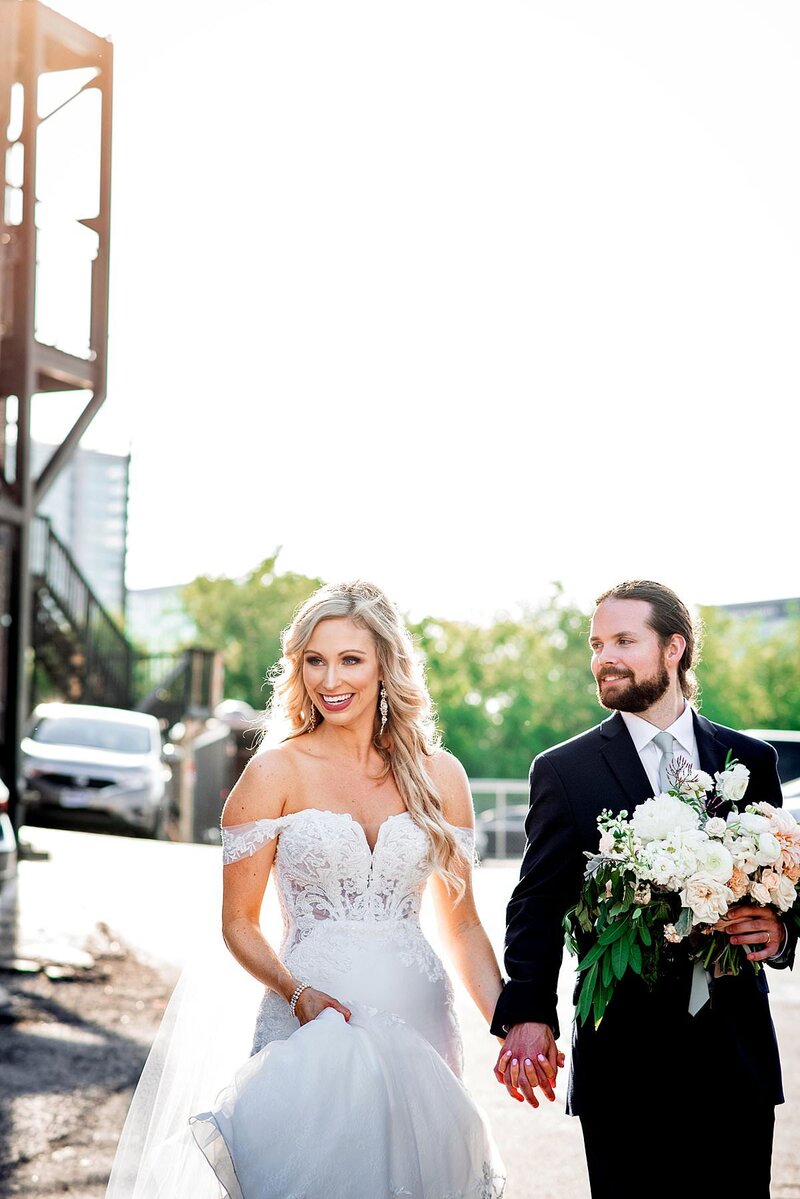 Bride and groom walking in the parking lot on their wedding day, holding hands and smiling