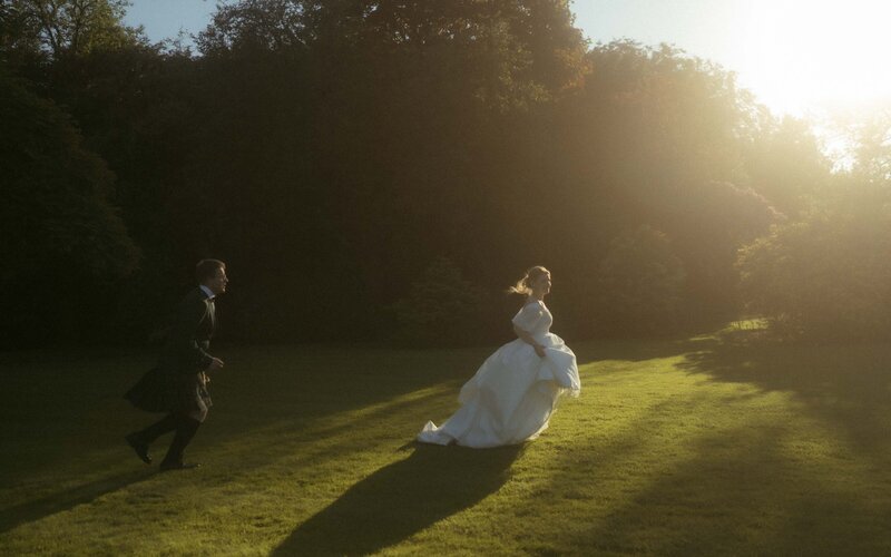 Couple playfully chasing each other on a grassy field during sunset, capturing carefree joy and golden-hour romance