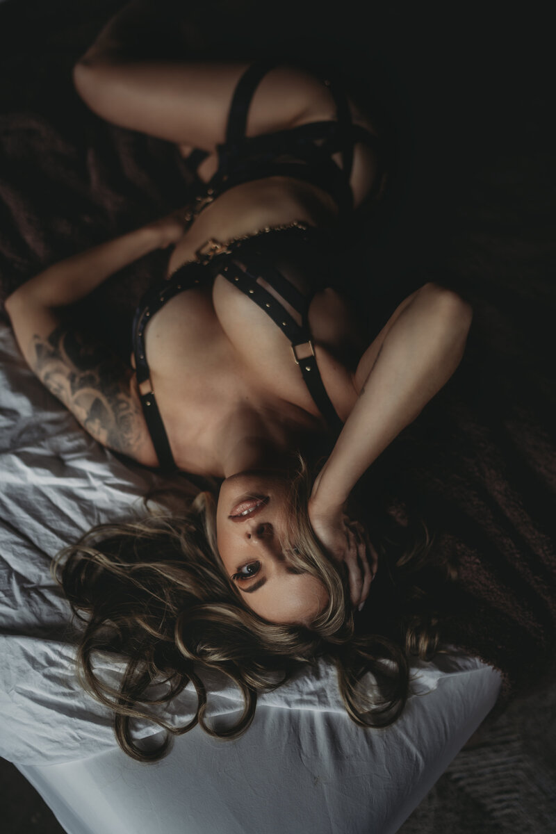 Boudoir portrait of a woman with long hair posing on a bed wearing black lingerie
