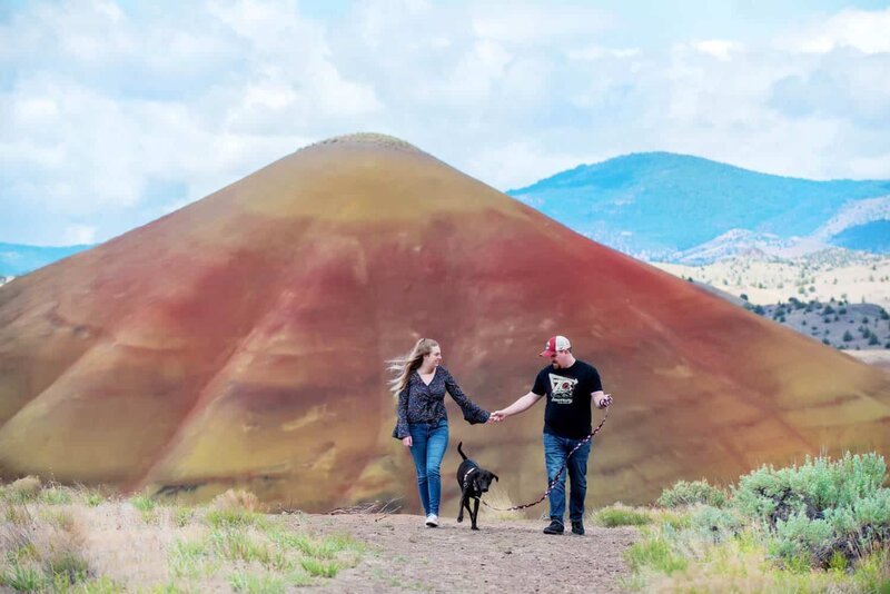 a couple walk with their dog in front of the painted hills during their engagement session