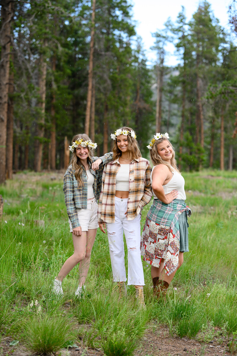 Senior photo outfit ideas of 3 girls standing in a mountain meadow with flannel shirts and flower crowns