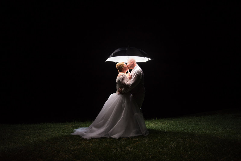 Bride with gorgeous ball gown style dress kissed groom under lit umbrella