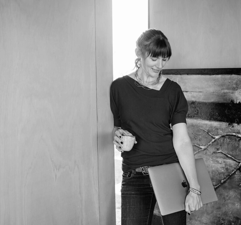 Sara Bower holding coffee leaning on wall inBlack and white