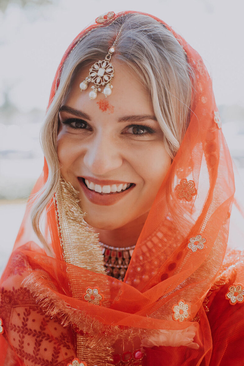 A bride wearing a vermillion sari smiles happily on her wedding day