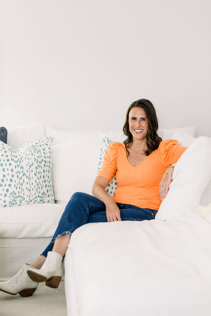 Digital Media Buying Expert Lara Murrant sitting on a white3 couch with orange shirt