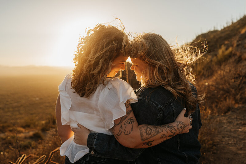 A couple with their arms around each other and their foreheads together at sunset 