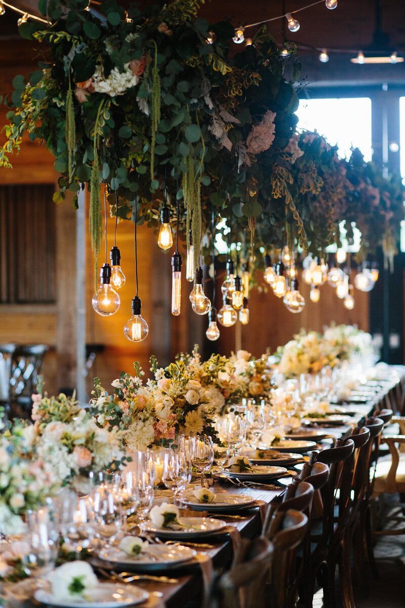 Greenery and exposed bulbs hanging over wedding reception head table