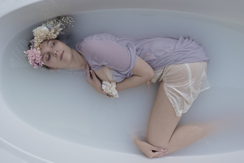 Girl in milk bath in vintage clothes with preserved flower headpiece and floral corsage  in pastel colours