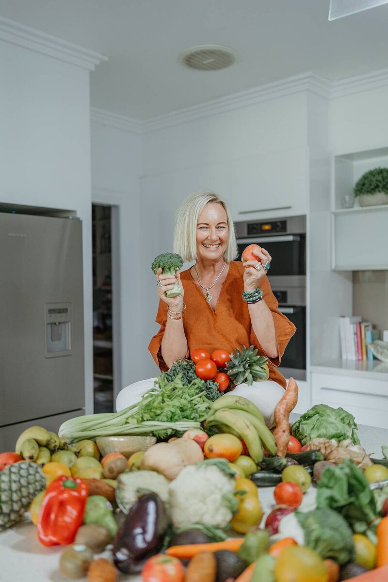 Branding photography capturing a business owner smiling while holding vegetables in her kitchen.