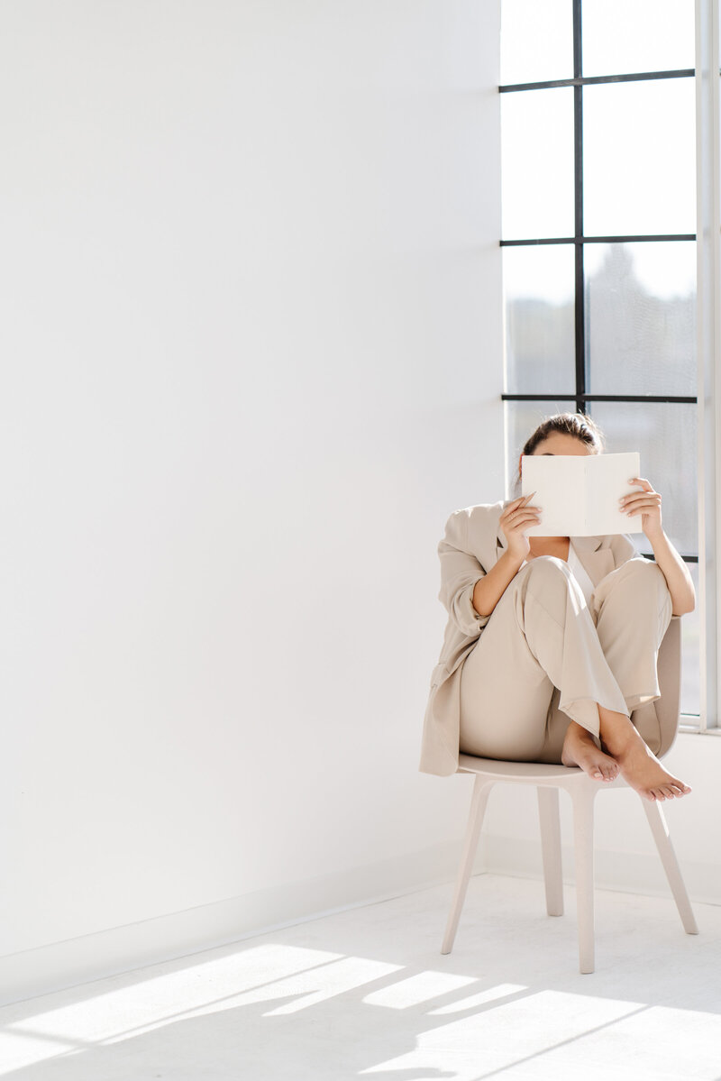 Woman in tan suit sitting on a stool reading a book