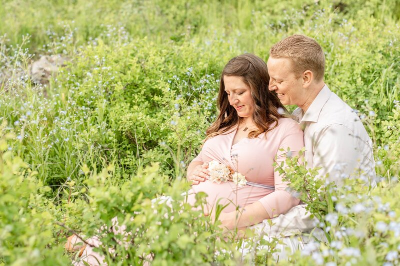 a pregnant woman sitting with her husband in a field