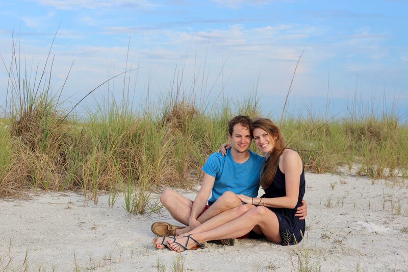 Couple sit together on beach looking at camera smiling naturally