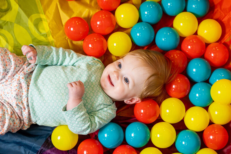 smiling infant laying down in a ball pit