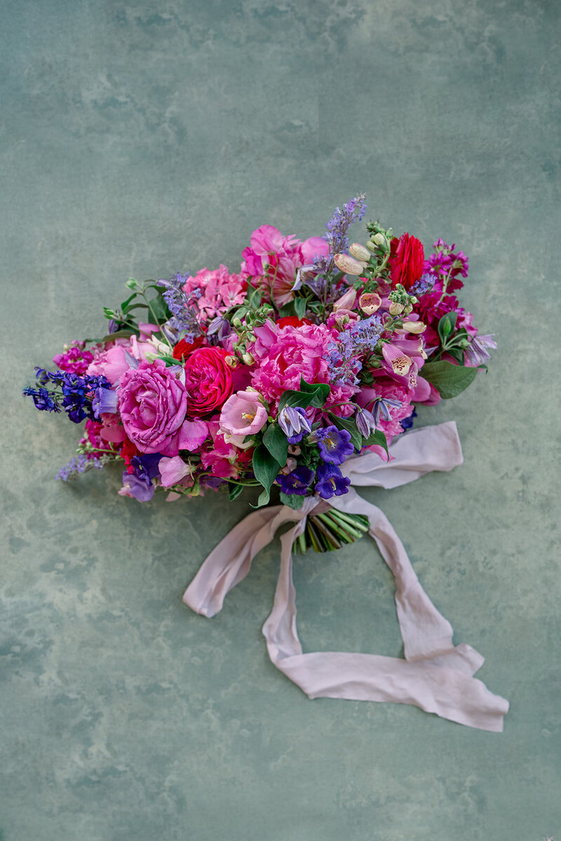 Colorful garden-style bridal bouquet with pink, lavender, and fuchsia florals captured in a film wedding photography flat lay in California.