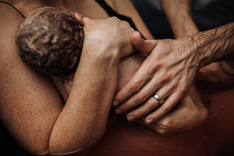 woman and man hands holding newborn