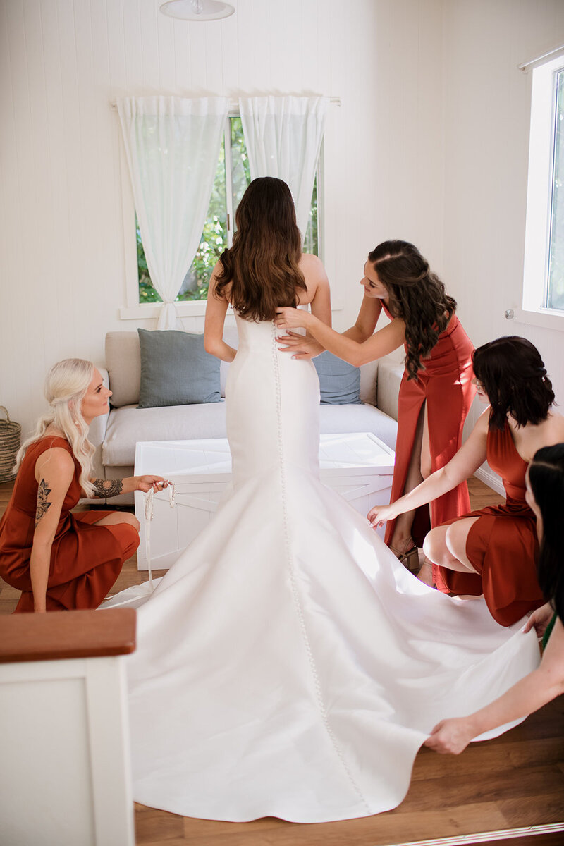 Bride assisted by her bridesmaids with her wedding dress
