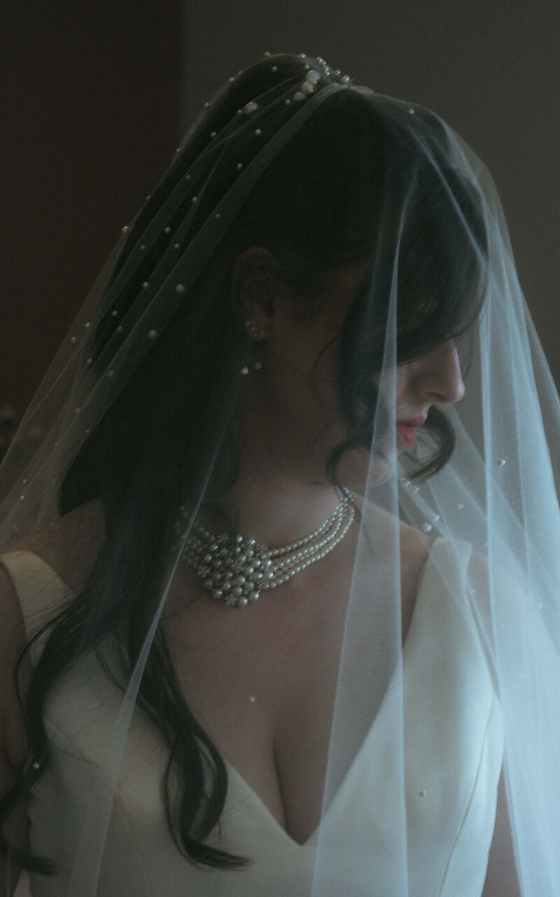 Bride gently resting under her veil, capturing a timeless moment of elegance and anticipation, as she prepares for the most beautiful day of her life