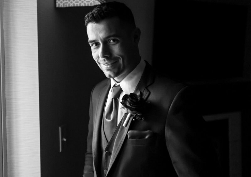 Solo portrait of groom standing in front of window and smiling at the camera